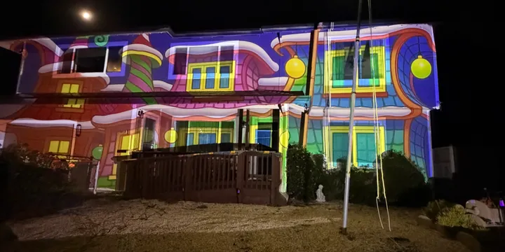 House transformed with bright, swirling candy land Christmas projections featuring bold colors, whimsical architecture, and glowing ornament balls.