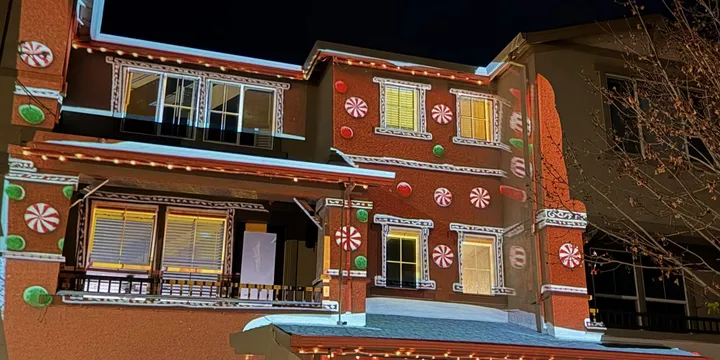 House transformed into a colorful gingerbread cottage with large gumdrop decorations and candy details projected across the façade.