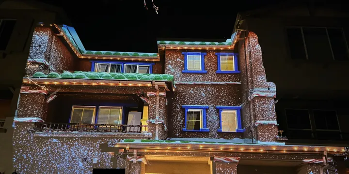 Projection of a cozy gingerbread house with frosted roofs and gently falling snow, creating a magical winter holiday scene on the home.