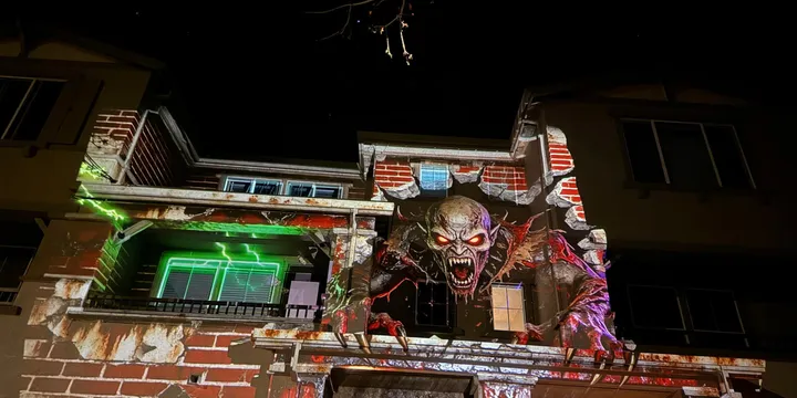 Projection mapping of a large, terrifying monster breaking through a brick wall on a house, claws reaching forward with dynamic shadows and lighting.