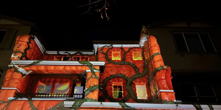House covered in animated glowing jack-o-lanterns and creeping vines, projected to look like Halloween decorations growing across the facade.